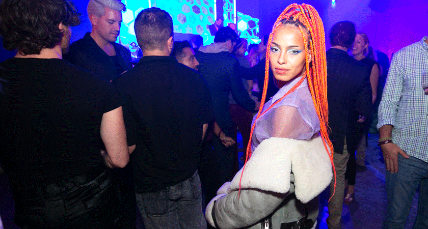 Guest poses at Penfolds House LA.  She wears a purple dress and a grey jacket.  She has long orange dreadlocks