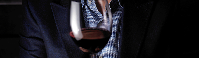 Person in blazer and blue shirt holds red wine glass
