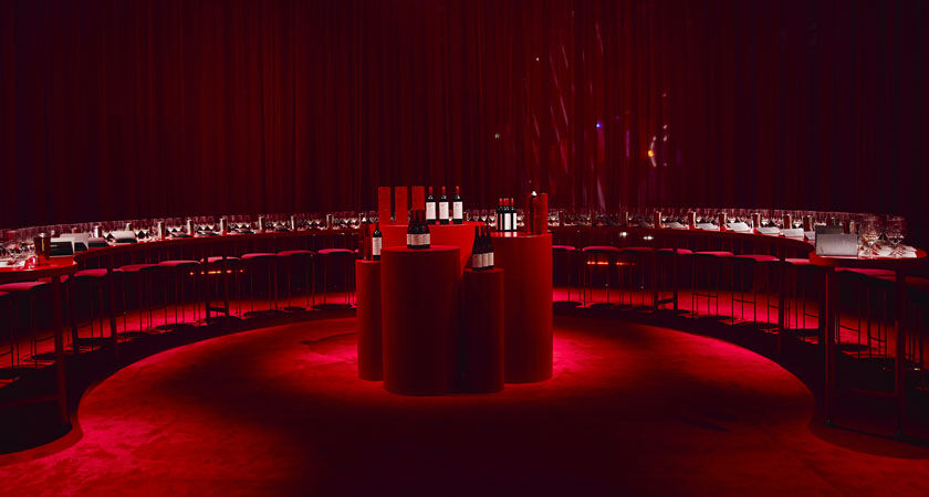 A red wine tasting room.  Semi circle table with bar stools and red plinths centred in front of table
