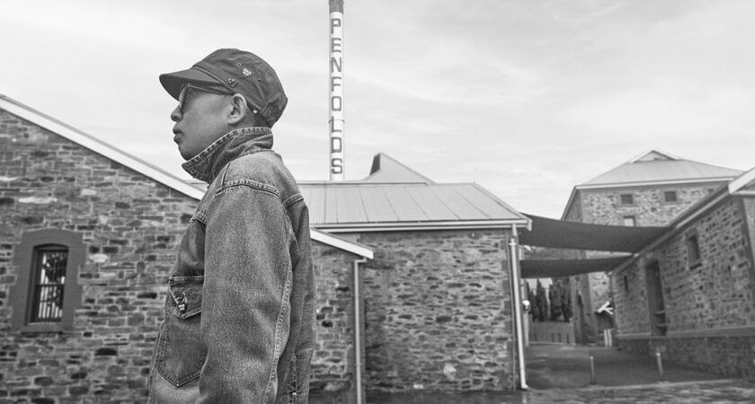 Black and white photo. Nigo stands in front of heritage brick building and Penfolds Magill Estate.